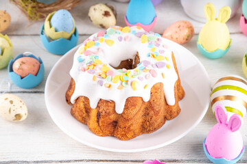 Traditional Easter cake decorated with sugar icing and sprinkles, with festive spirit decor and flower bouquet. Easter celebrations holiday table with pastel colored Easter eggs and bunny rabbits