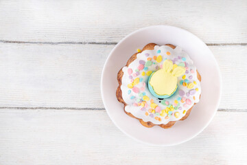 Traditional Easter cake decorated with sugar icing and sprinkles, with festive spirit decor and flower bouquet. Easter celebrations holiday table with pastel colored Easter eggs and bunny rabbits