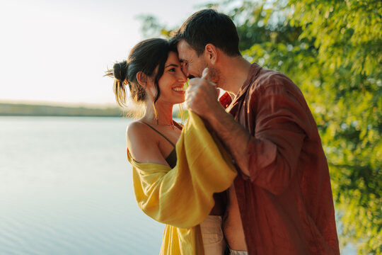 Happy couple dancing by the lake at sunset, enjoying romantic moment