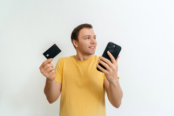 Young handsome man thinking about online shopping via internet, holding credit card and smartphone isolated on white background