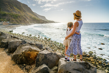 A mother and her young daughter stand on the rocky shore of Playa del Socorro, Tenerife, as...