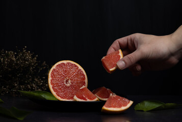 Male hand holding a grapefruit slice lying on a black plate on a dark background, citrus fruit with diuretic properties