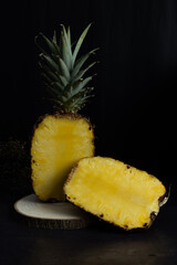 Vertical image of a halved pineapple on a wooden log on a rustic background, fragrant and sweet tropical fruit. dark food