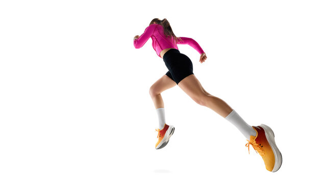 Low angle view of young female runnier in motion, running, showing progress, movement, and athletic ambition against white background. Concept of athletics, sport, endurance, healthy lifestyle. Ad