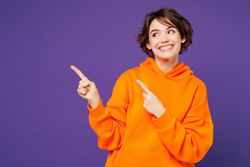 Young smiling fun happy Caucasian woman she wear orange hoody casual clothes point index finger...