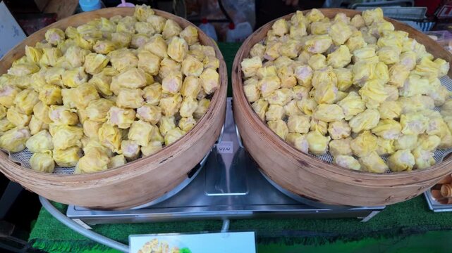 Batch of freshly steamed Kanom Jeeb Thai dumplings sits in traditional bamboo baskets at a bustling street food stall wrapped in wonton skins and filled with a savory mixture of minced pork and shrimp