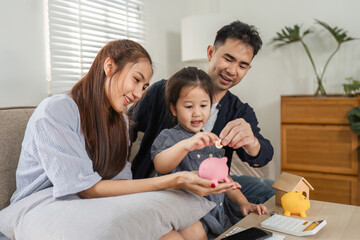 Parents teaching their daughter about saving money with piggy banks at home.