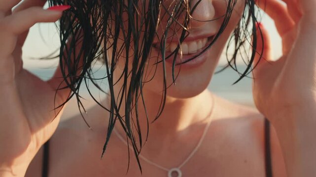 Happy young woman with wet hair smiles and runs her fingers through her hair on the beach at sunset.