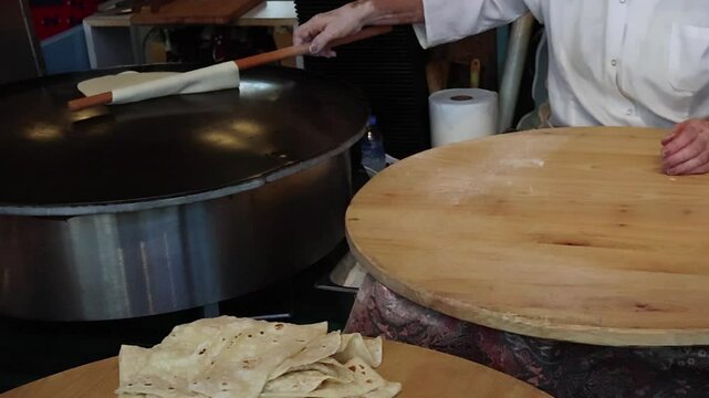 Woman in white uniform preparing traditional Turkish Gozleme on hot griddle. Street food concept with fresh handmade flatbreads