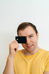 Cheerful young man, studio portrait. People sincere emotions lifestyle concept. Mock up copy space. Covering eye with credit bank card.
