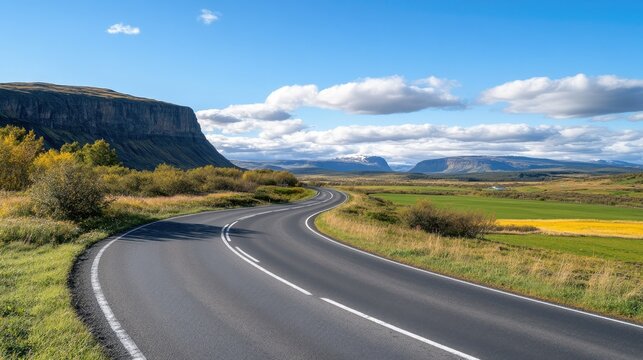 Scenic winding road through lush green landscape in Iceland under a bright blue sky with fluffy clouds