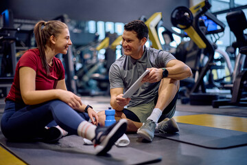 Happy coach and athletic woman using digital tablet during sports training in gym.