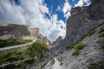 Hikers navigate rocky trails in the majestic Dolomites of Italy on a clear day with dramatic cloud formations