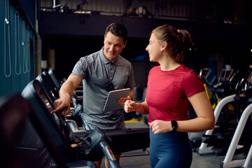 Happy personal trainer and athletic woman during her run on treadmill in gym.