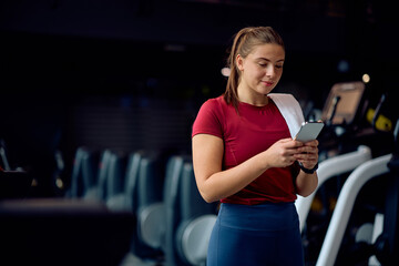 Fototapeta premium Young sportswoman using app on smart phone while working out in gym.