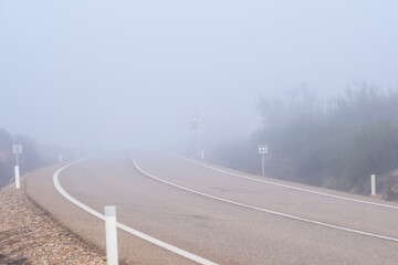 Deserted road disappearing into dense fog, evoking a sense of mystery and isolation.