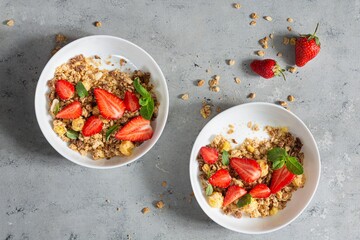 Homemade crunchy granola with nuts, dried fruits, fresh strawberries, mint and yogurt (fermented baked milk) on a white plate. Healthy breakfast concept.