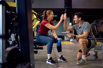 Happy sportswoman and her personal coach giving high-five in gym.