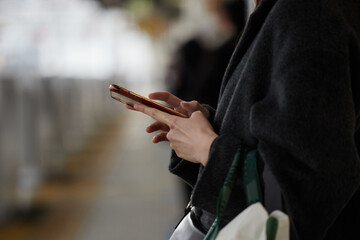 携帯電話をいじる女性が駅のホームで電車待ちの様子