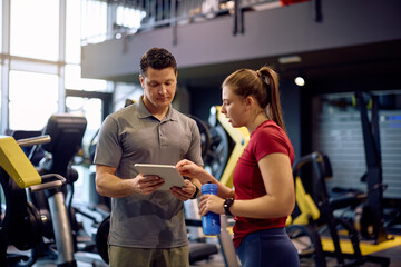 Personal coach and young sportswoman using touchpad during exercise class at health club.