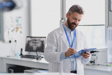 Doctor in doctors office reading medical records in clipboard.