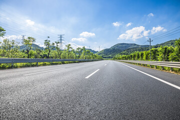Empty asphalt road through landscape with clear sky and green mountain