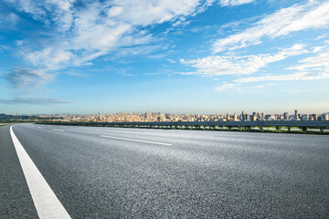 Asphalt road leading to city skyline against blue sky with clouds