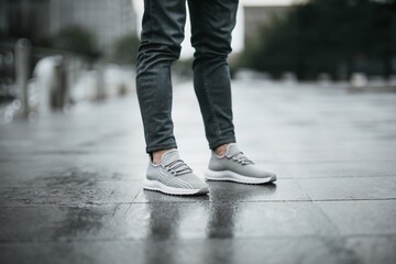 Man wearing gray sneakers standing on wet pavement