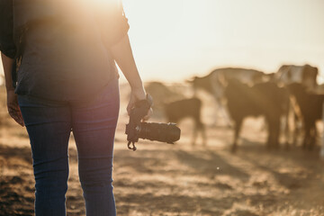 Woman standing in a dusty and dry grassy paddock holding a digital camera
