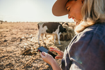 Woman holding and looking through her phone smiling on farm