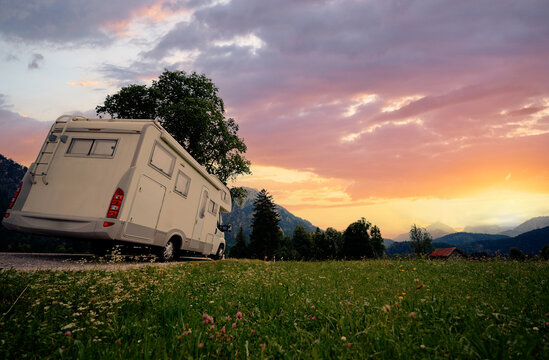A white camper van is parked on a scenic rural road under a sunset sky, with lush greenery surrounding it. Ideal for concepts of travel and adventure