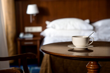 A white cup of hot tea or coffee on a wooden table in the interior of a hotel room. The concept of drinks and comfortable hotel accommodation.