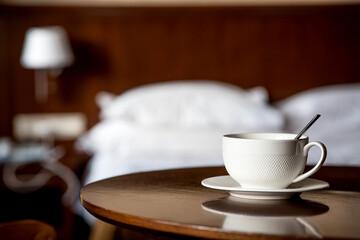 A white cup of hot tea or coffee on a wooden table in the interior of a hotel room. The concept of drinks and comfortable hotel accommodation.