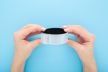 Young adult woman hand fingers holding and showing light gray reflective tape on light blue table...