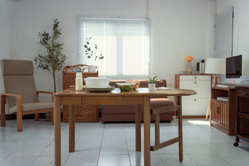 Wooden dining table with healthy food, milk and salad, in a cozy and bright living room with sofa, armchair, plants and computer, ideal for a quiet and comfortable life