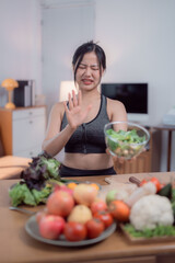 Young woman wearing sportswear is showing disgust for a bowl of salad while preparing a healthy...