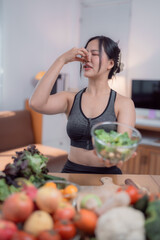 Young sporty woman pinching her nose with disgust while holding a bowl of salad, refusing to eat...