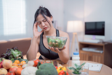 Young sportswoman suffering headache while holding a bowl of salad and having healthy food such as...