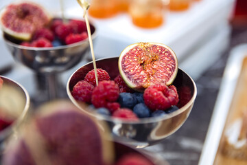 A polished silver bowl is filled with a variety of fresh berries and figs