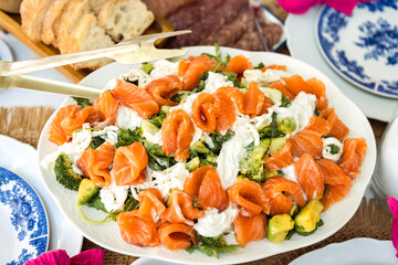 A fresh tasty salmon salad is served with avocado and creamy dressing. Slices of pink salmon top the greens and vegetables.
