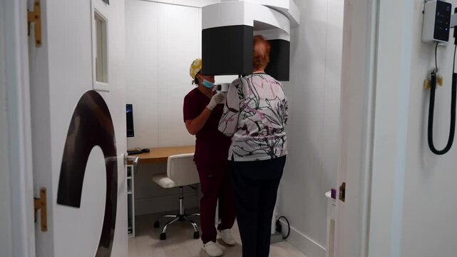 Old woman with head inside X-ray machine for dental scan as dentist sets it up