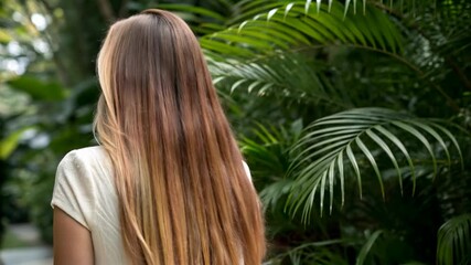 woman with long blonde hair turning in slow motion in tropical greenery, wind blowing through her hair, beauty and nature footage