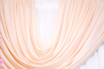 A beautifully draped peach-colored fabric with a soft flowing texture on a white background, ideal for weddings or event decorations
