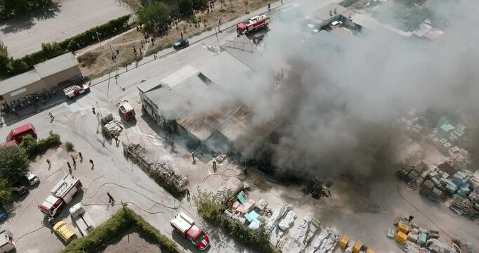 Industrial fire aftermath  Firefighters work to suppress residual flames among burnt pallets blackened rubble. Yard shows clear signs destruction emergency response