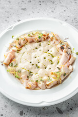 A gourmet dish featuring a smooth, creamy base surrounded by thinly sliced cured meat and garnished with fresh herbs, presented on a stylish white plate against a minimalist backdrop.
