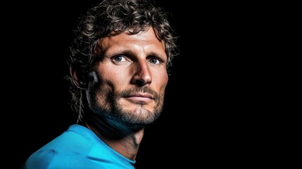 Obraz premium Male athlete poses with an intense expression, showcasing strength and perseverance. The contrasting blue shirt stands out against the dark backdrop, emphasizing his features