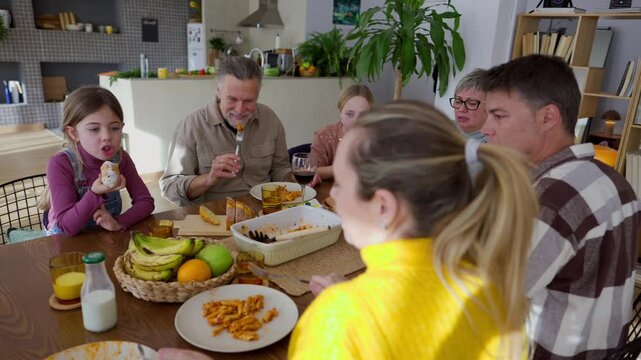 Grandparents, parents, and children gather around a dining table, sharing a meal and engaging in lively conversation, creating a warm and joyful family atmosphere
