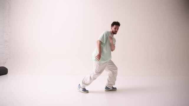 Young artistic man dressed casual, oversized stylish outfit, dance freestyle in motion against white studio background. Concept of art and sport, music, creativity, fashion and style.