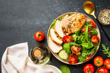 Green salad with grilled chicken meat at black table. Top view with copy space.