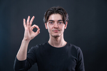 The handsome young man showing ok sign with his fingers with a selective focus on isolated black...